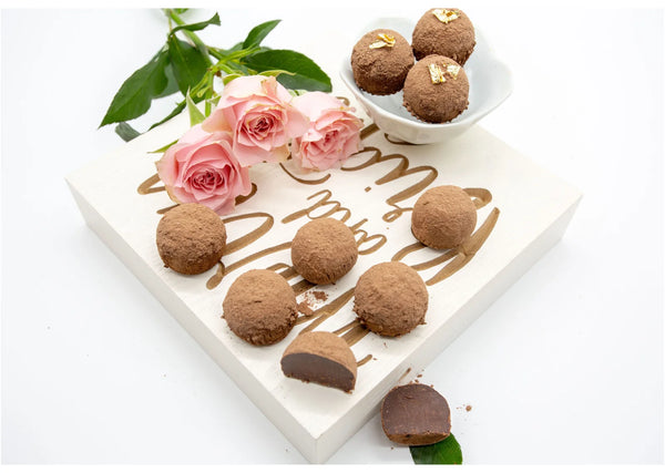 Classic Milk Truffles made with milk chocolate ganache and hints of Madagascar vanilla on a white table with pink roses