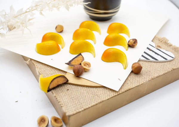 Hazelnut Caramel yellow handpainted dark chocolate bonbons with a hazelnut praline filling on a white table