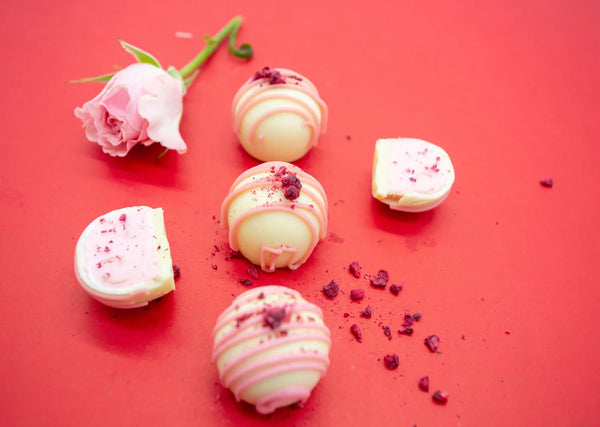 Indulgence Truffles on a red background with white chocolate shell and pink Ruby chocolate stripes and creamy pink raspberry white chocolate ganache