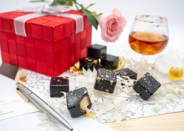 Irish Cream dark chocolate bonbons with orange splattered paint and Baileys creamy filling, on a white table next to a red gift box and whiskey cocktail
