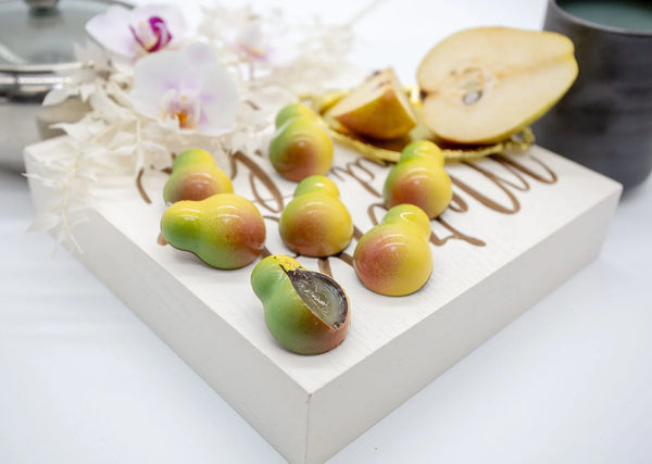 Pear Caramel pear-shaped dark chocolate bonbons with yellow, green, and red coloring and a pear jam caramel filling on a white table with sliced pear