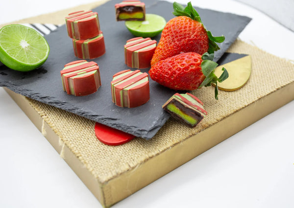 Strawerry Lime pink and green dark chocolate bonbons with sliced lime and strawberries on a table