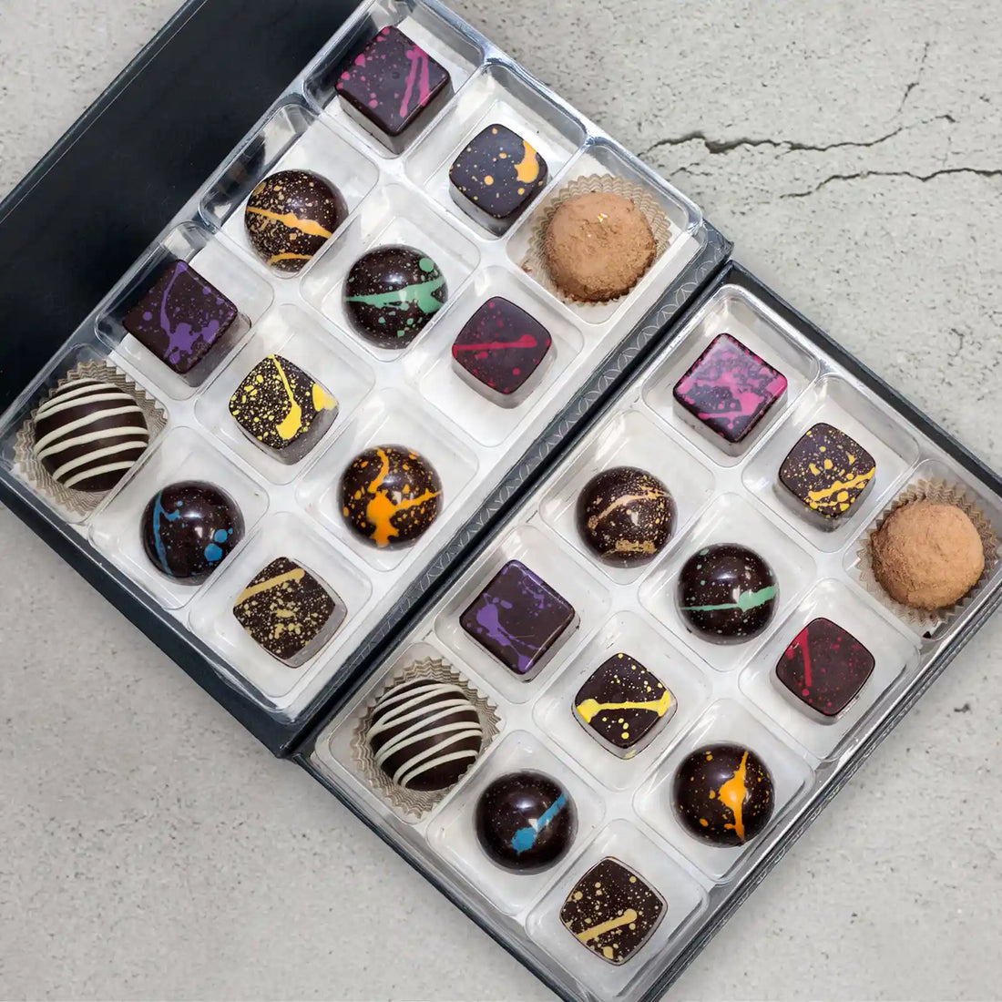 Enchantment Elite 24-piece chocolate gift box showing the 12 flavors of sugar free dark chocolates with a rainbow of splattered paint and 2 truffles