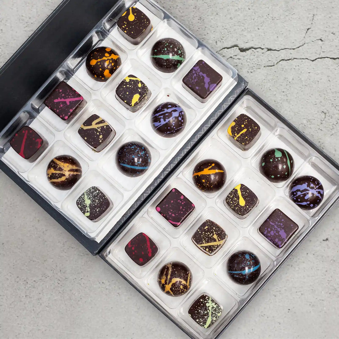 Miranda Elite 24-piece chocolate gift box showing the 12 flavors of sugar free dark chocolates with a rainbow of splattered paint