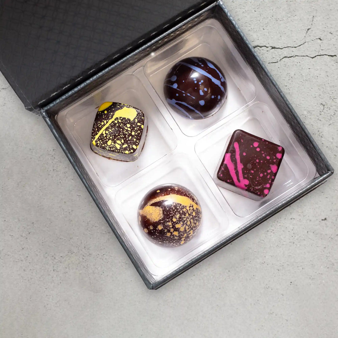 4-piece Elite Collection gift box with 4 dark chocolate bonbons splattered with yellow, orange, purple, and pink