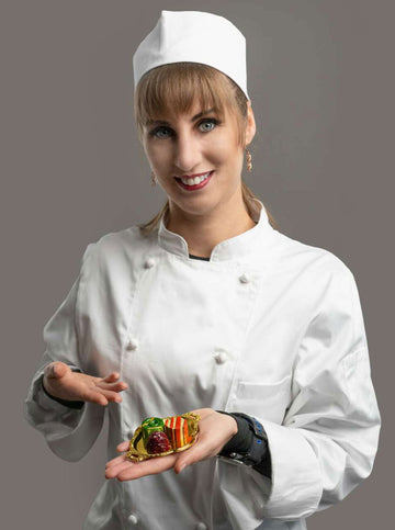 Beata in chef uniform holding a small gold plate with 3 brightly colored chocolate bonbons