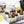Dulce de Cream dark chocolate dome-shaped bonbons with orange splattered paint and milky vanilla filling on a white table next to white flowers, vanilla plant, an a teapot