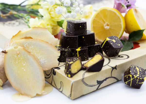Lemon Curd dark chocolate bonbons with yellow splattered paint and creamy yellow lemon filling on a white table with sliced lemon and pear