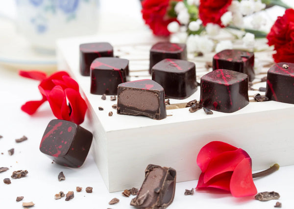 Molten Chocolate dark chocolate bonbon with red splattered paint and creamy ganache filling on a white table with red roses
