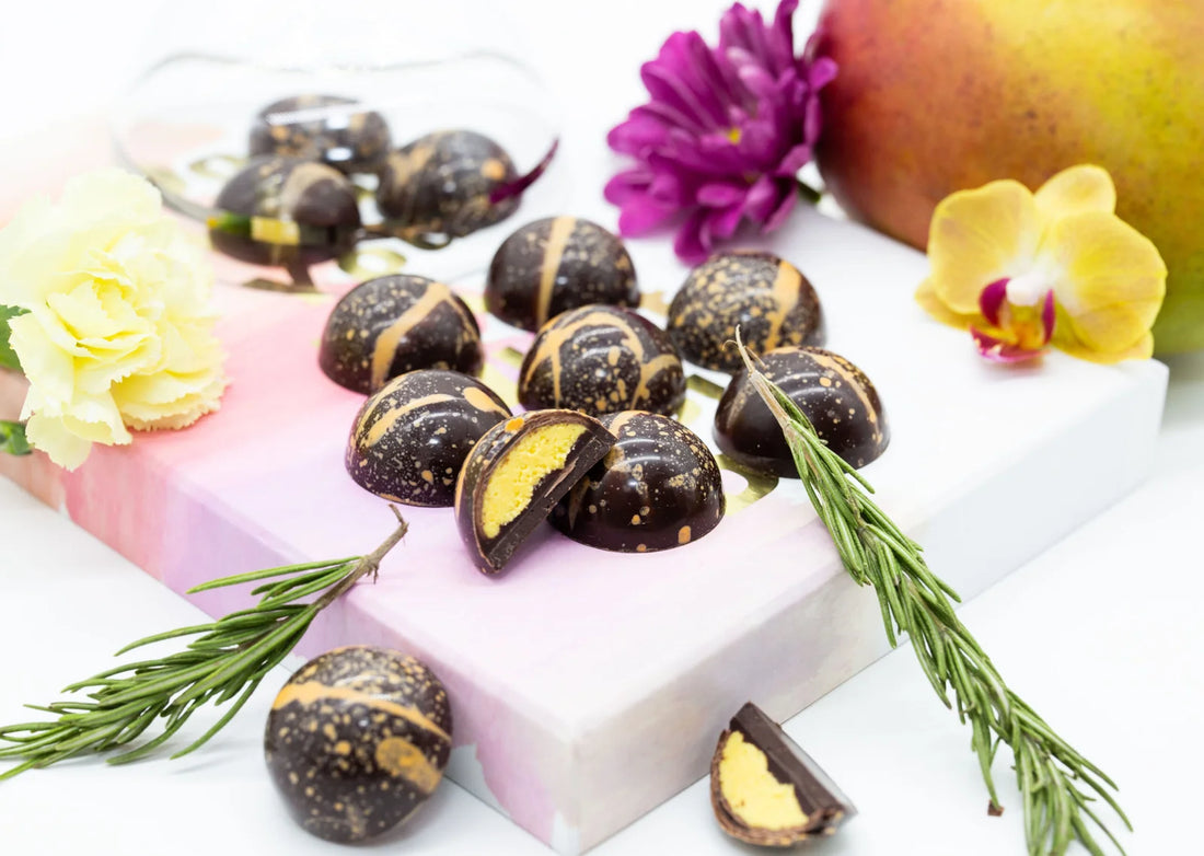 Rosemary Mango dome-shaped sugar free dark chocolate bonbon with orange splattered paint