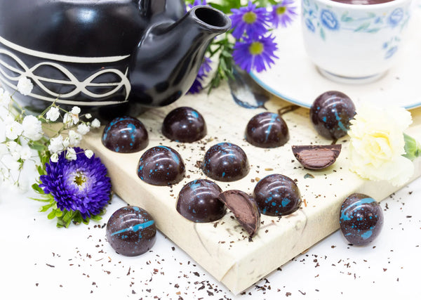 Spicy Earl Grey dark chocolate bonbons with blue splattered paint sitting beside teapot and cup of tea surrounded by flowers
