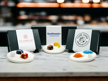 Chocolate gift boxes showing custom branded logos set beside colorful chocolate bonbons on a white marble countertop