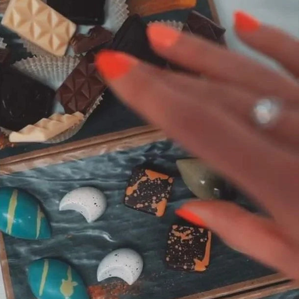 Close up of woman's hand reaching for a display of luxury chocolate bonbons and truffles